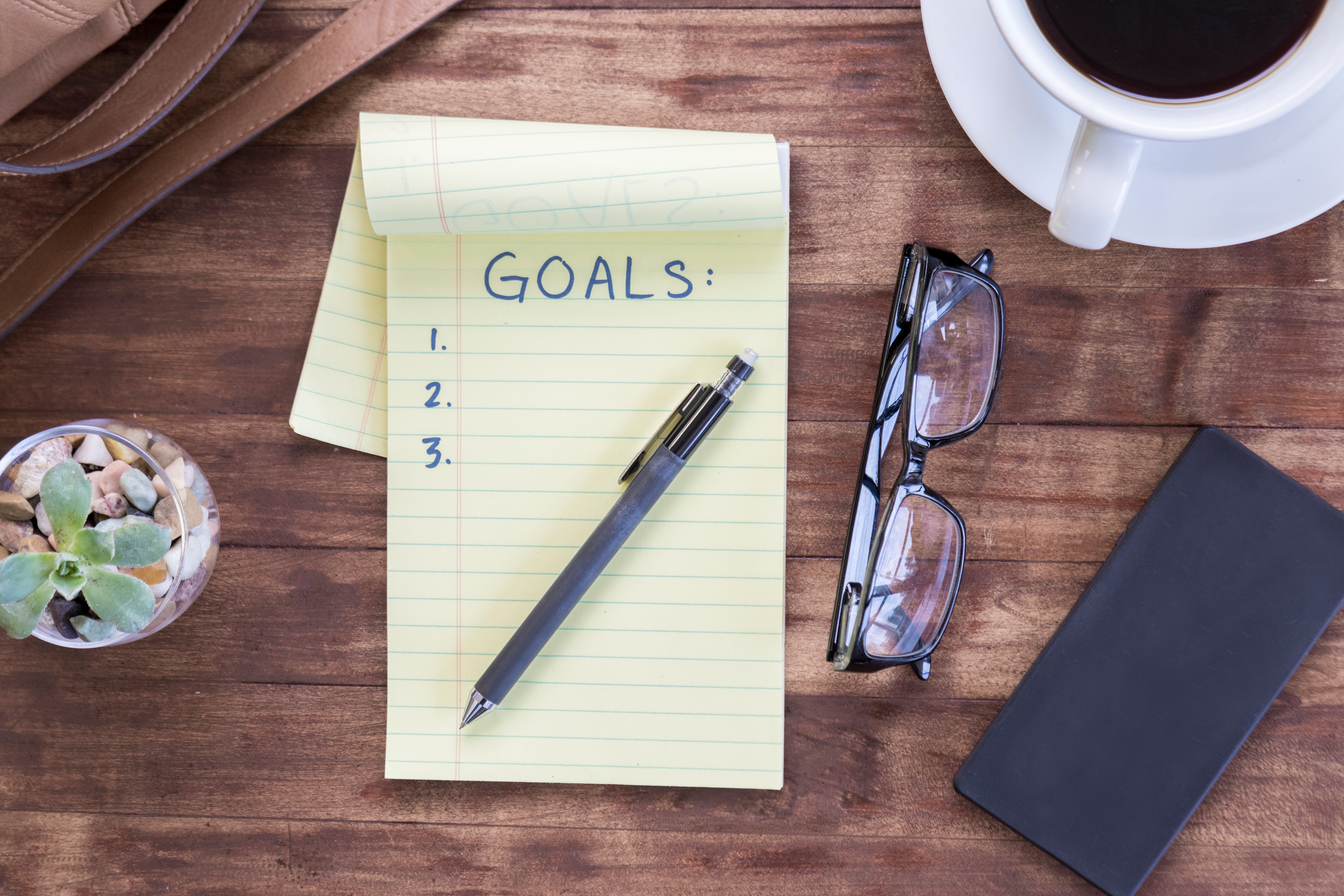 notepad that says goals and a pen on a desk-1